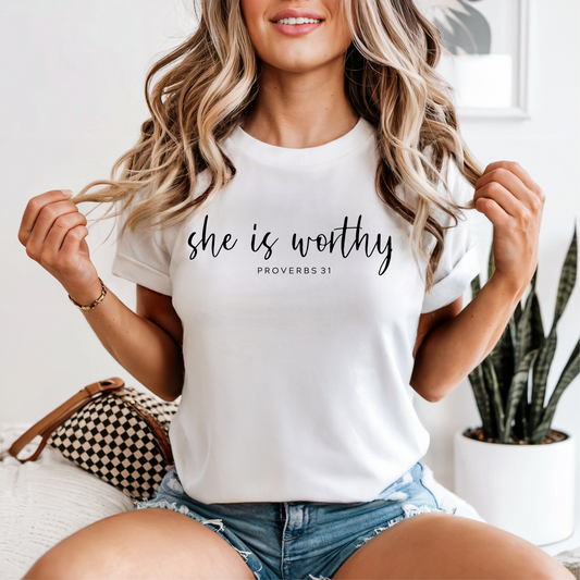 Woman wearing a white t-shirt with 'she is worthy Proverbs 31' text, sitting on a couch.